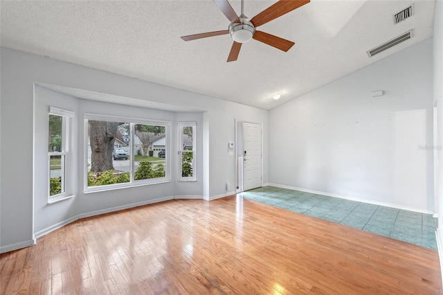 empty room featuring ceiling fan, vaulted ceiling, a textured ceiling, and light wood-type flooring