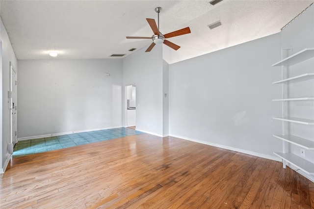 spare room featuring ceiling fan, vaulted ceiling, light hardwood / wood-style floors, and a textured ceiling