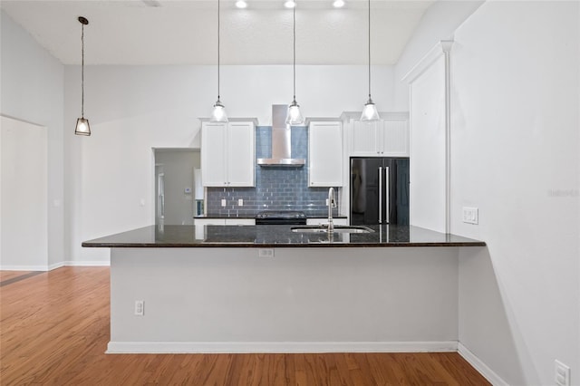 kitchen featuring wall chimney range hood, high quality fridge, sink, and white cabinets