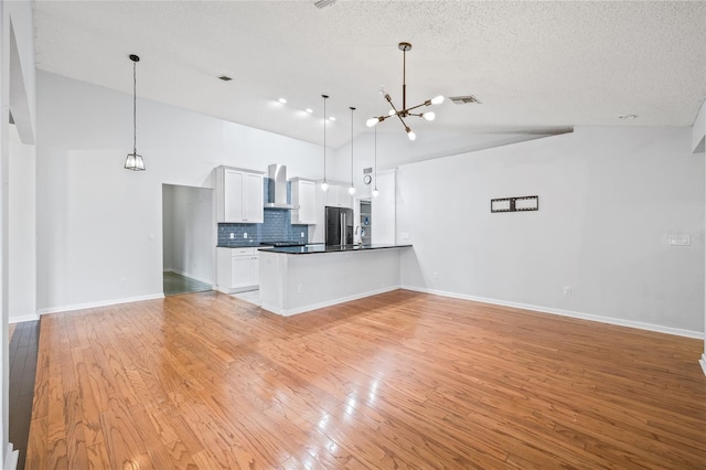 kitchen with high end fridge, a chandelier, hanging light fixtures, white cabinets, and wall chimney range hood