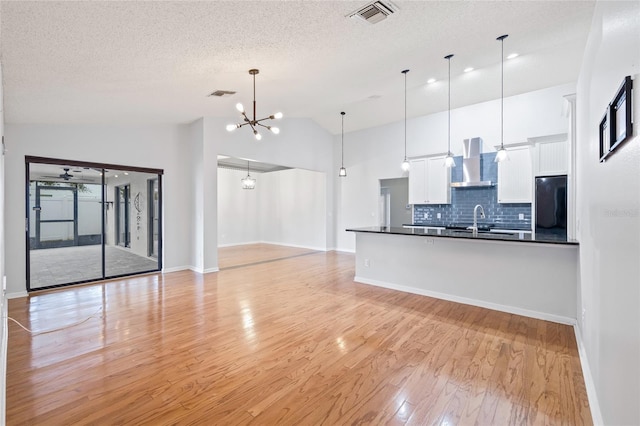 interior space featuring pendant lighting, wall chimney range hood, sink, white cabinetry, and black fridge