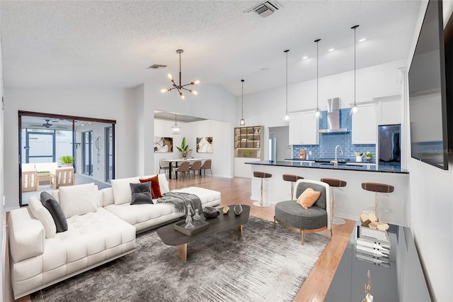 living room with hardwood / wood-style floors, high vaulted ceiling, sink, a notable chandelier, and a textured ceiling