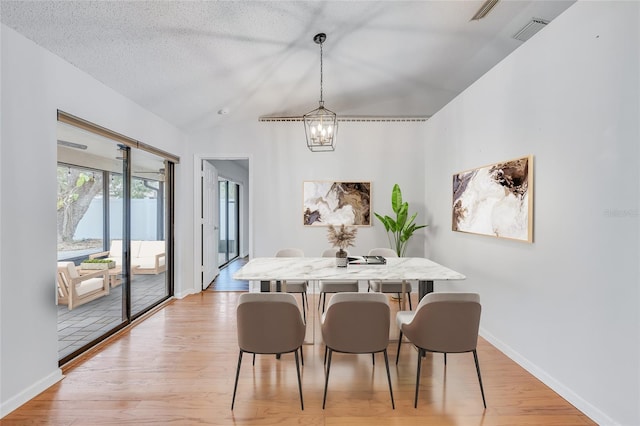 dining room featuring an inviting chandelier, light hardwood / wood-style floors, a textured ceiling, and lofted ceiling