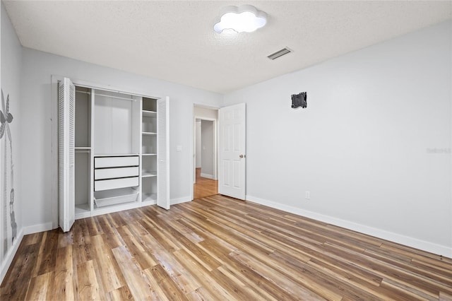 unfurnished bedroom with wood-type flooring, a closet, and a textured ceiling