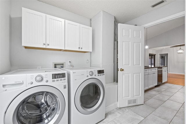 clothes washing area with light tile patterned floors, washing machine and dryer, cabinets, and a textured ceiling