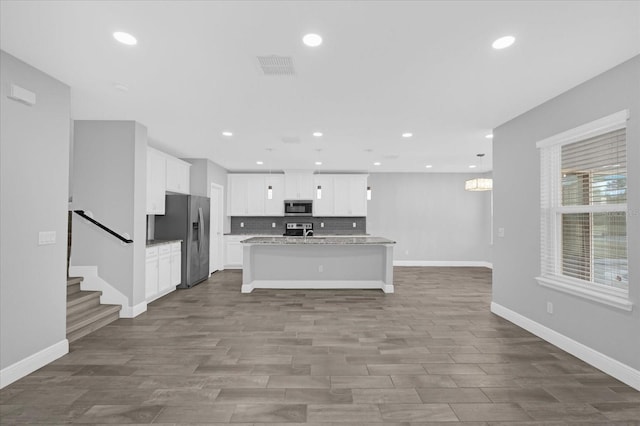 kitchen featuring tasteful backsplash, an island with sink, white cabinets, light stone counters, and stainless steel appliances