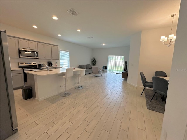 kitchen featuring gray cabinetry, stainless steel appliances, a center island with sink, decorative light fixtures, and light wood-type flooring