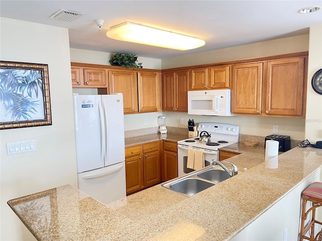 kitchen featuring sink, white appliances, a kitchen breakfast bar, light stone counters, and kitchen peninsula