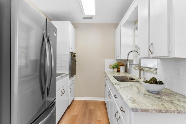 kitchen featuring sink, white cabinetry, light wood-type flooring, appliances with stainless steel finishes, and light stone countertops