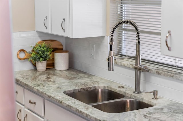 room details with tasteful backsplash, sink, light stone counters, and white cabinets