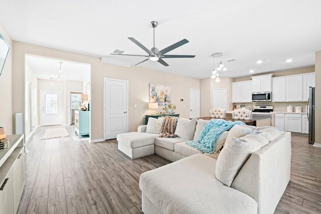 living room with ceiling fan with notable chandelier and light wood-type flooring