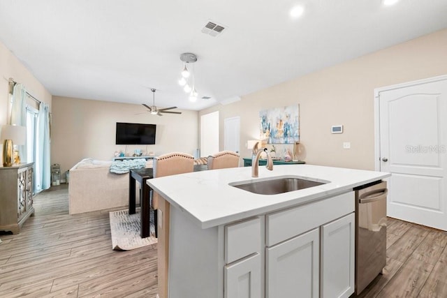 kitchen featuring dishwasher, sink, a kitchen island with sink, ceiling fan, and light wood-type flooring