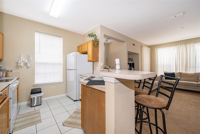 kitchen featuring a breakfast bar, a wealth of natural light, sink, kitchen peninsula, and white appliances