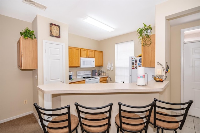 kitchen featuring a breakfast bar, sink, white appliances, and kitchen peninsula