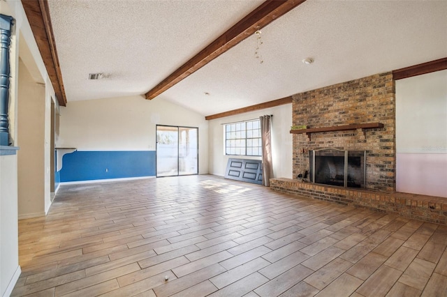 unfurnished living room featuring a brick fireplace, vaulted ceiling with beams, a textured ceiling, and light hardwood / wood-style flooring