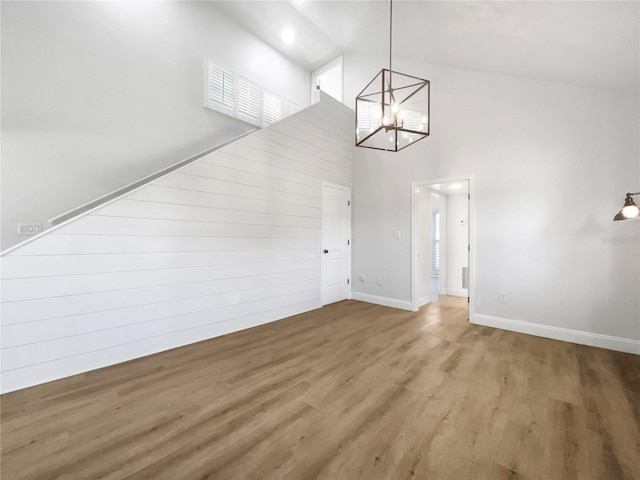 unfurnished living room featuring an inviting chandelier, hardwood / wood-style floors, wooden walls, and high vaulted ceiling