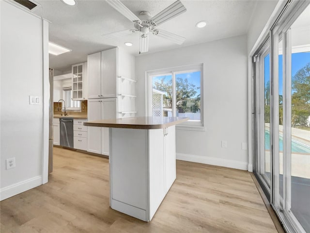 kitchen featuring white cabinetry, sink, a kitchen breakfast bar, stainless steel dishwasher, and light hardwood / wood-style flooring