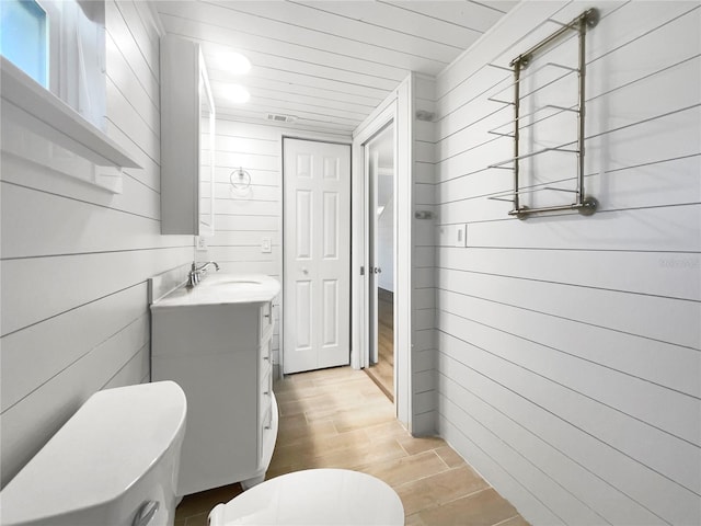 bathroom featuring vanity, wood-type flooring, wooden walls, and toilet