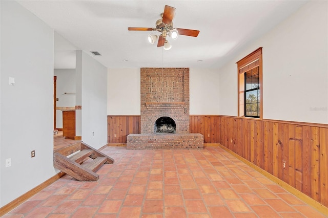 unfurnished living room with ceiling fan, a fireplace, and wood walls