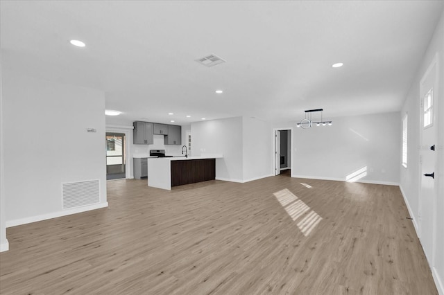 unfurnished living room with a healthy amount of sunlight, sink, a chandelier, and light hardwood / wood-style floors