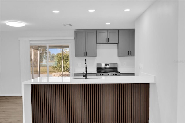 kitchen with sink, stainless steel range with electric stovetop, gray cabinets, kitchen peninsula, and hardwood / wood-style flooring