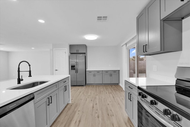 kitchen with gray cabinetry, sink, light wood-type flooring, and appliances with stainless steel finishes