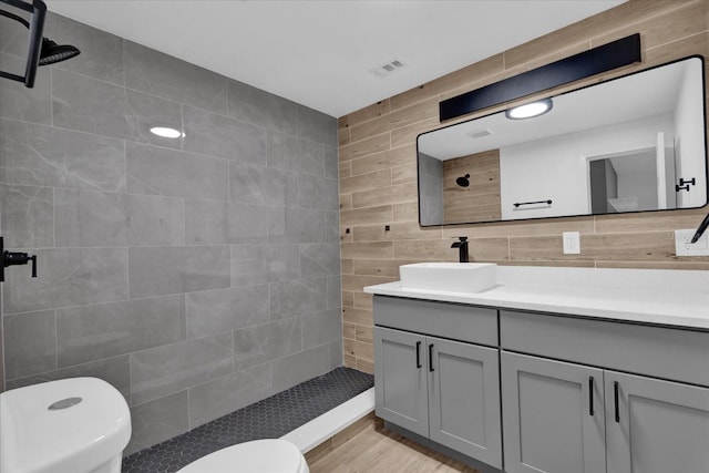 bathroom with vanity, tile walls, toilet, and tiled shower