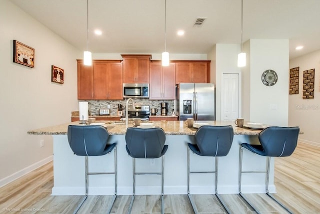 kitchen with appliances with stainless steel finishes, a breakfast bar area, hanging light fixtures, and backsplash