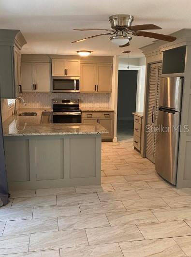 kitchen with appliances with stainless steel finishes, stone countertops, sink, decorative backsplash, and kitchen peninsula