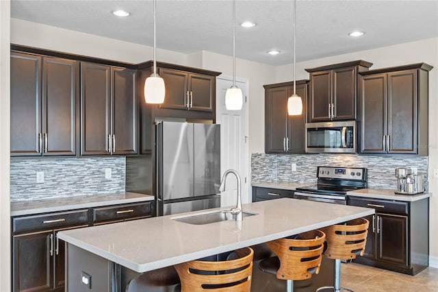 kitchen with sink, appliances with stainless steel finishes, a kitchen breakfast bar, a center island with sink, and decorative light fixtures