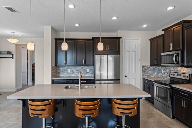 kitchen with pendant lighting, stainless steel appliances, and a center island with sink