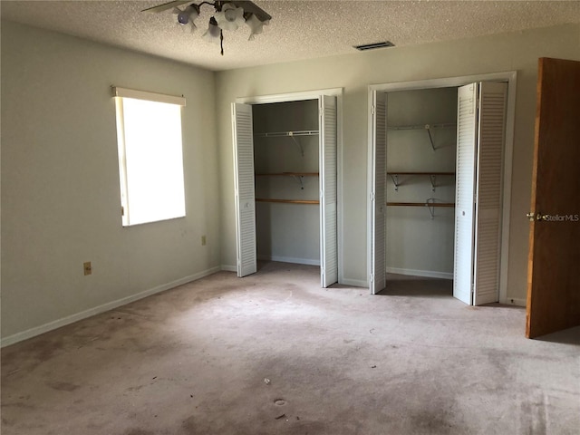 unfurnished bedroom with light carpet, a textured ceiling, and two closets