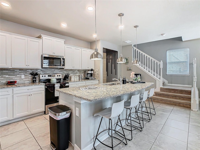 kitchen with white cabinetry, hanging light fixtures, light tile patterned floors, an island with sink, and stainless steel appliances