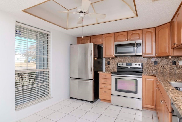 kitchen with tasteful backsplash, a raised ceiling, appliances with stainless steel finishes, light tile patterned flooring, and light stone countertops