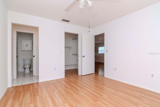 unfurnished bedroom featuring baseboards, visible vents, a walk in closet, a textured ceiling, and light wood-style floors