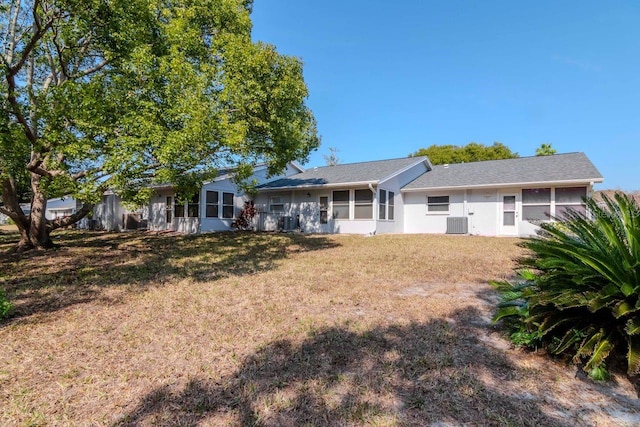 rear view of house with central AC unit and a lawn