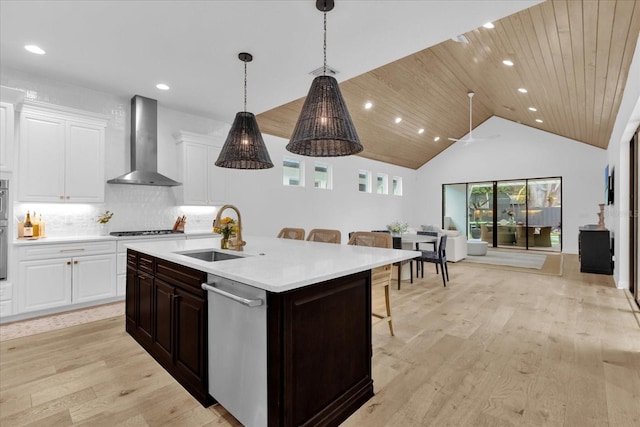 kitchen with wall chimney exhaust hood, sink, a center island with sink, a kitchen breakfast bar, and dishwasher