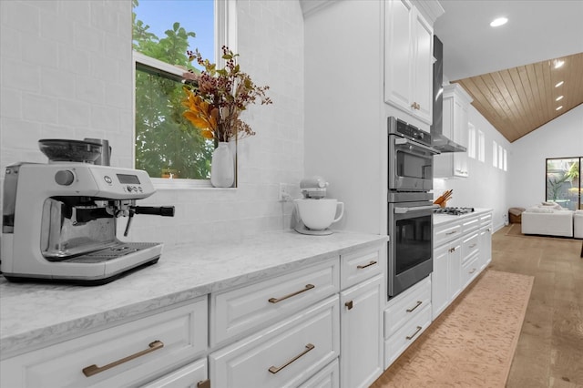 kitchen featuring lofted ceiling, light hardwood / wood-style flooring, white cabinets, light stone countertops, and backsplash