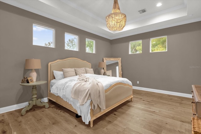 bedroom with an inviting chandelier, a tray ceiling, and light hardwood / wood-style flooring