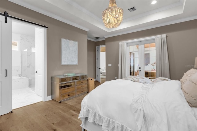 bedroom featuring light hardwood / wood-style flooring, ornamental molding, a raised ceiling, and a barn door