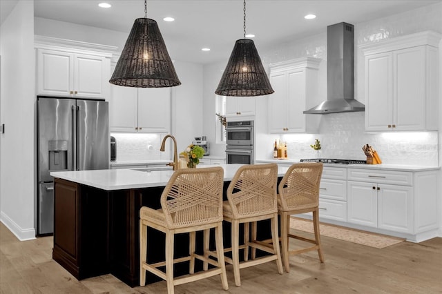 kitchen featuring wall chimney range hood, sink, appliances with stainless steel finishes, a kitchen island with sink, and white cabinets