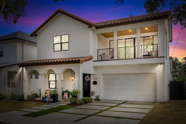 mediterranean / spanish-style house with driveway, a balcony, a tiled roof, an attached garage, and stucco siding