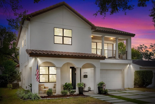 view of front of home with a balcony, a tile roof, an attached garage, and stucco siding