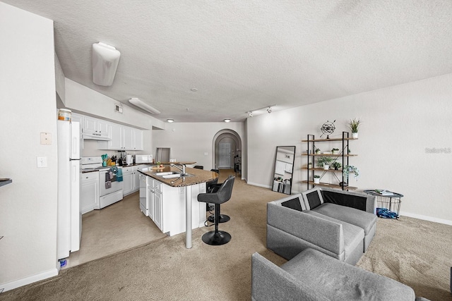 kitchen featuring sink, white cabinets, a kitchen breakfast bar, a center island with sink, and white appliances