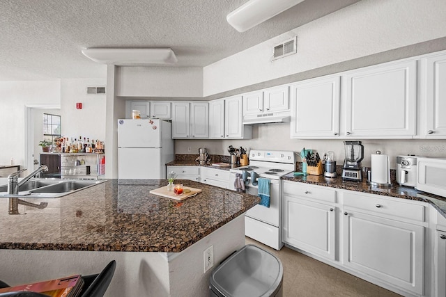 kitchen featuring sink, white appliances, white cabinetry, a textured ceiling, and dark stone counters