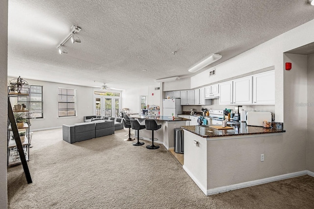 kitchen with white cabinetry, white appliances, light colored carpet, and kitchen peninsula