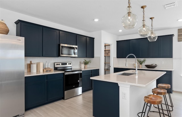 kitchen featuring a kitchen bar, sink, appliances with stainless steel finishes, pendant lighting, and a kitchen island with sink