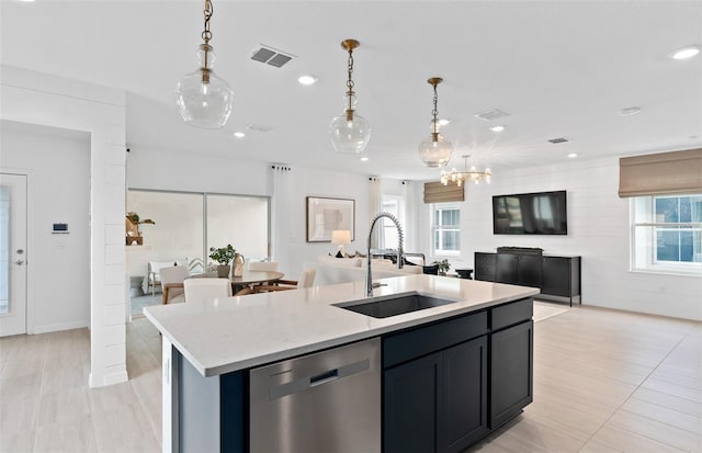 kitchen featuring sink, decorative light fixtures, stainless steel dishwasher, an island with sink, and light stone countertops