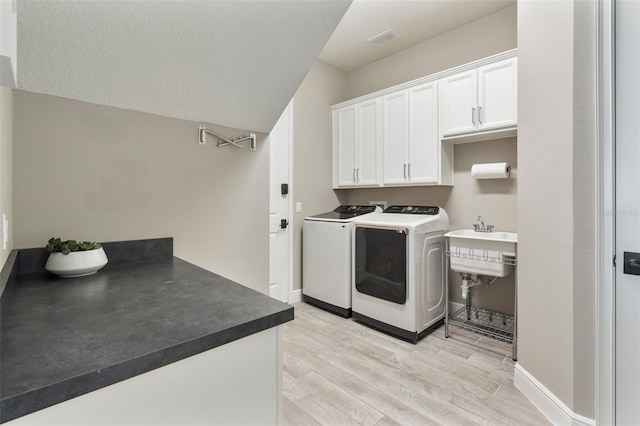 washroom featuring cabinets, a textured ceiling, washer and clothes dryer, and light hardwood / wood-style floors