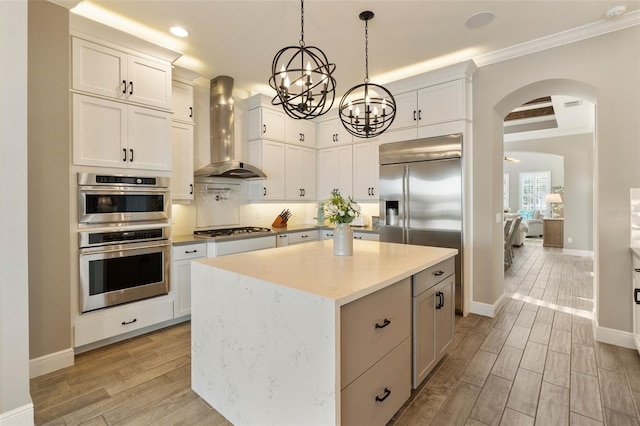 kitchen with wall chimney range hood, a kitchen island, white cabinets, and appliances with stainless steel finishes